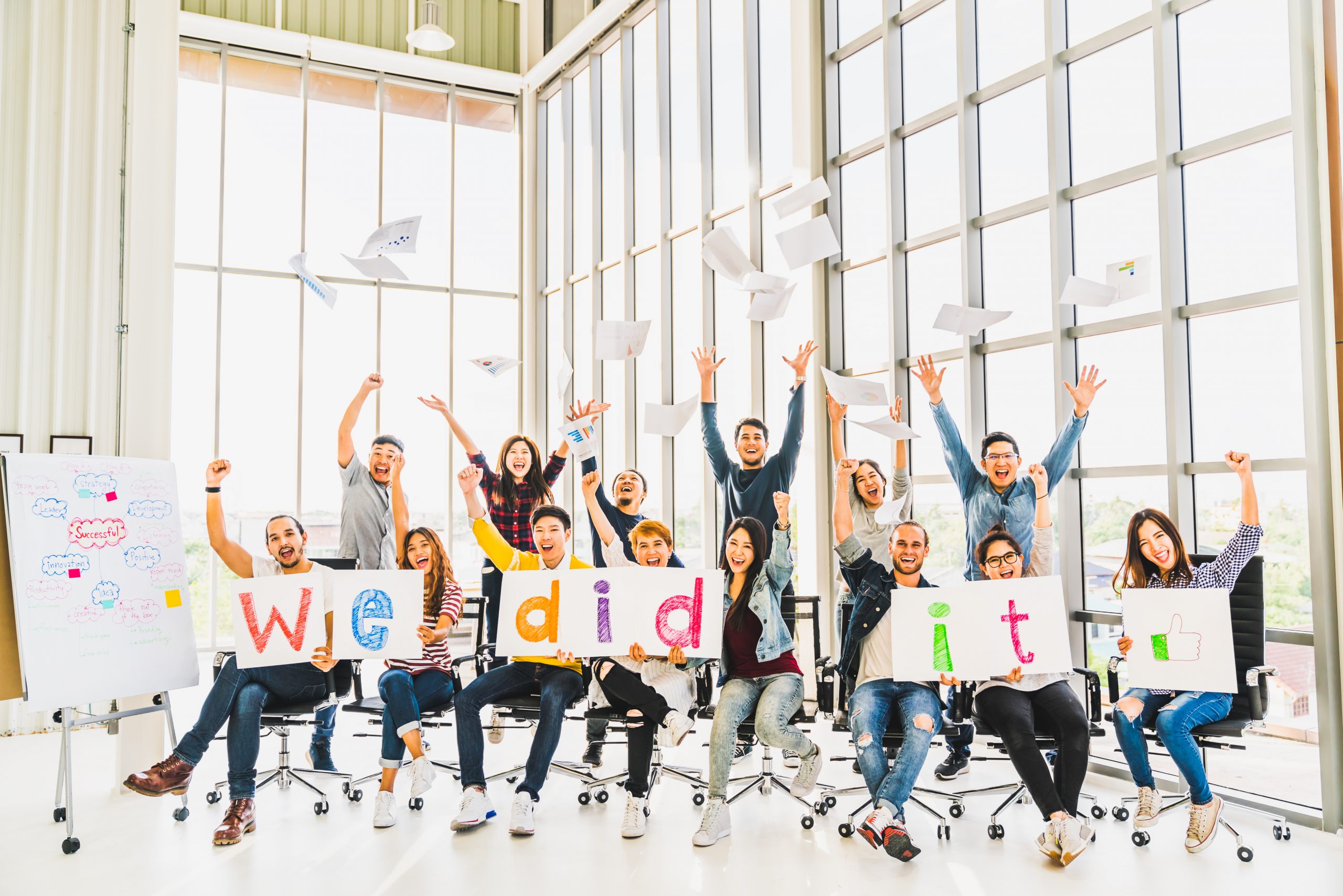 Multiethnic diverse group of happy business people cheering together, celebrate project success with papers wrote words We did it. Coworkers teamwork, career job achievement, or small business concept